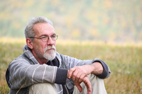Older man with a concerned expression sitting in a field