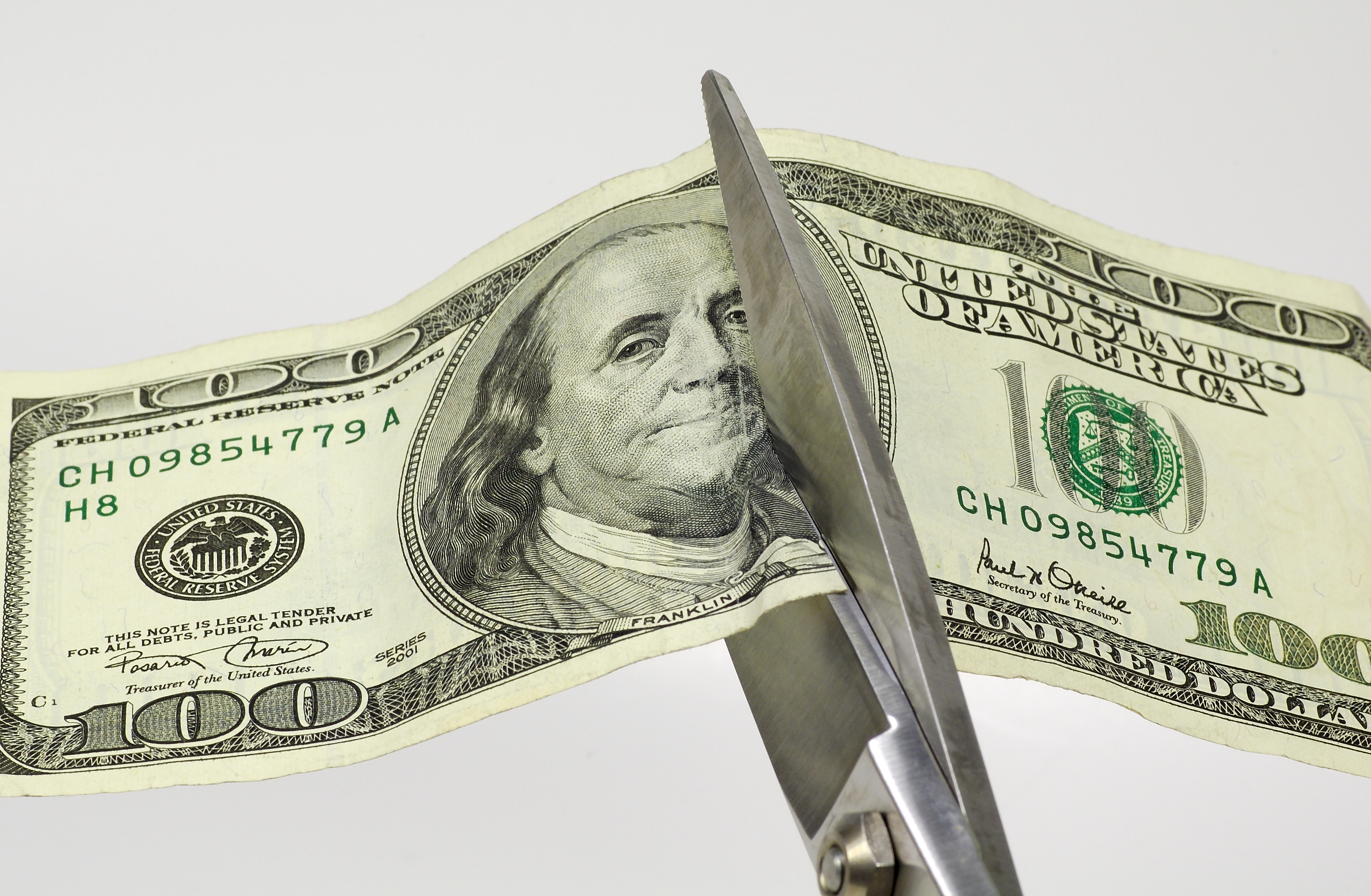 A hundred dollar bill being cut in half by scissors.