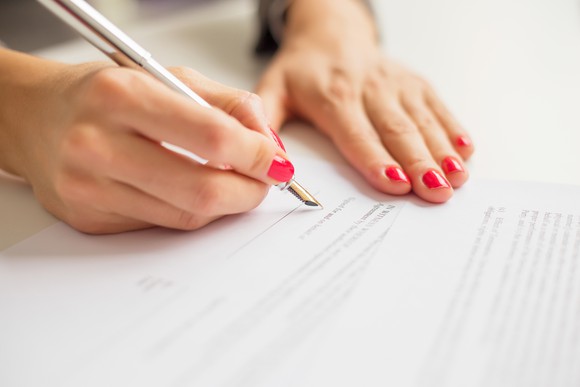 A person with red nail polish on signs a paper with a fountain pen.