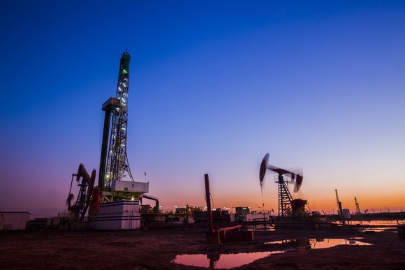 Drilling rig next to several pumpjacks at sunset.