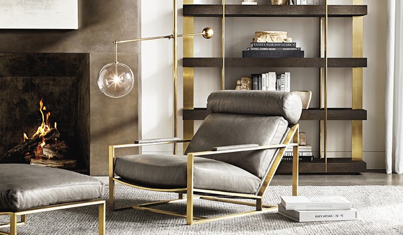 Large chair with ottoman in front of fireplace next to lamp and shelves, all in a modern style.