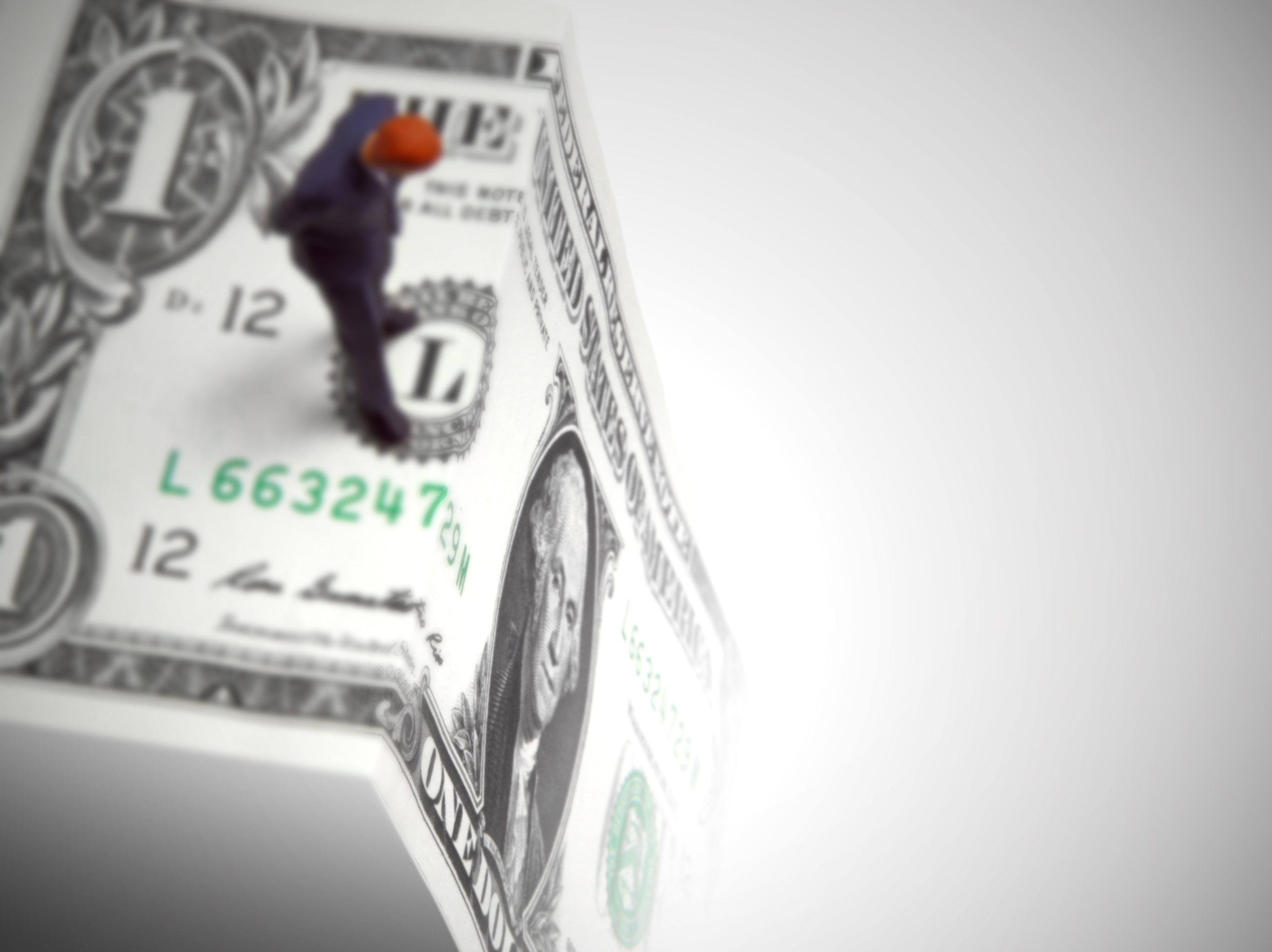Man standing on edge of folded $1 bill