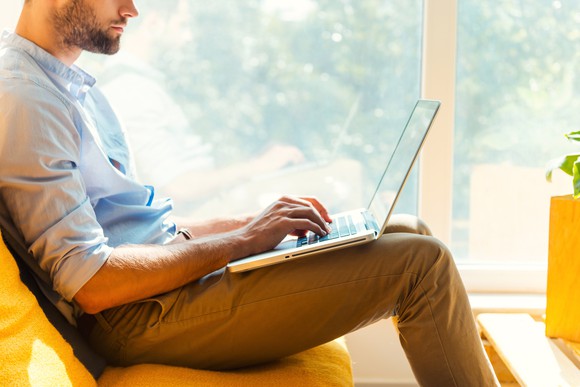 A man uses a laptop on a couch.