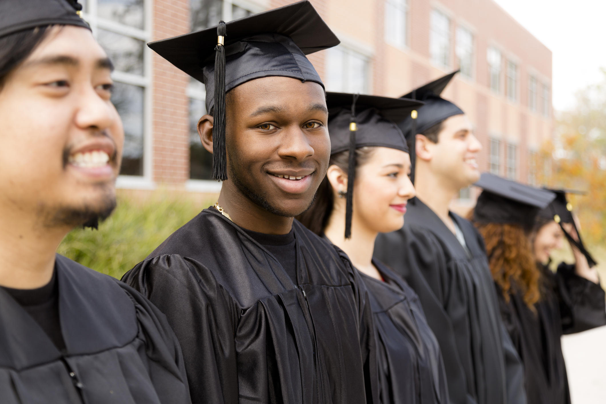Several smiling grads in black gowns at a college setting.
