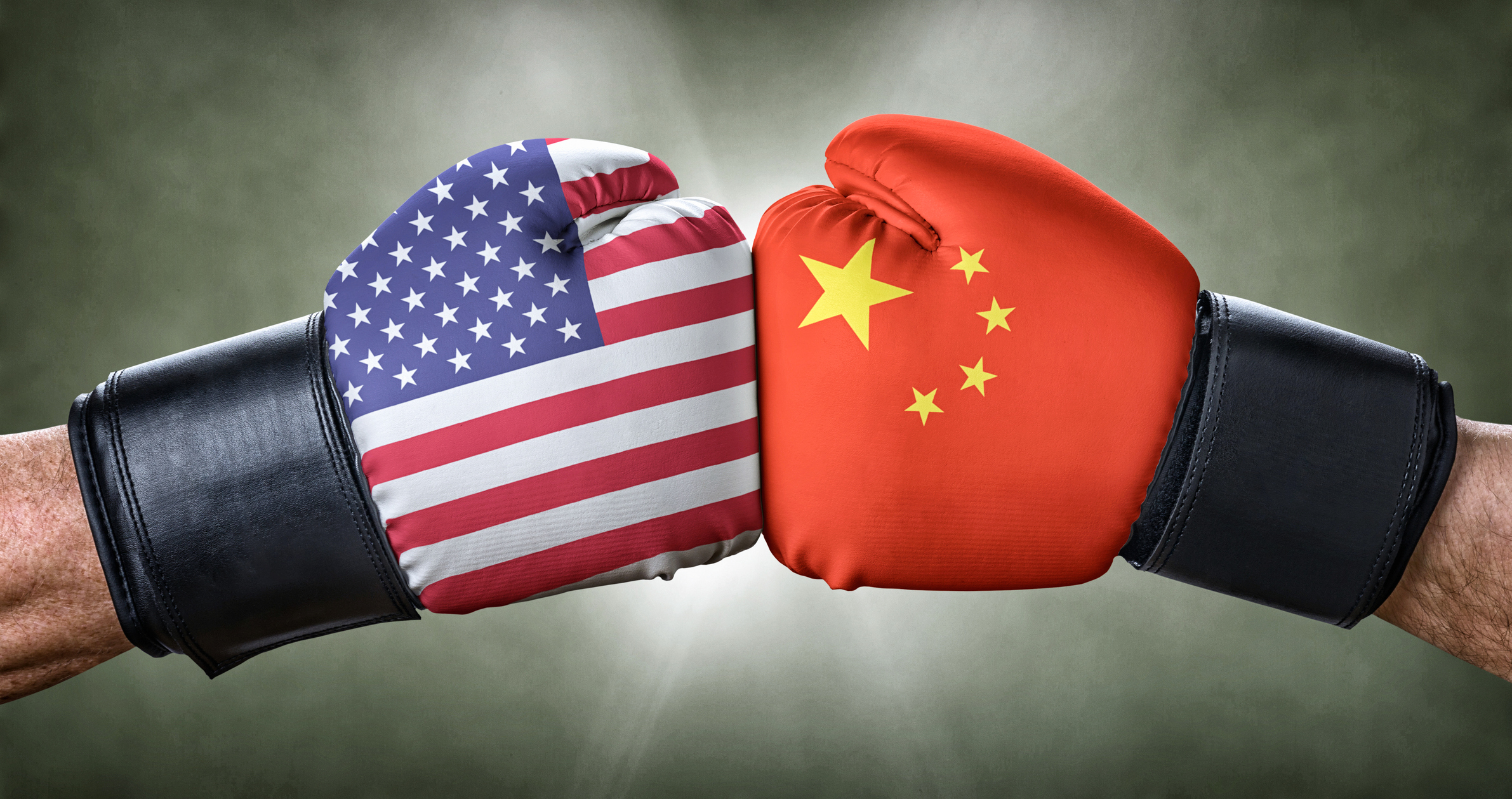 The hands of two different people wearing boxing gloves, with the US and China flags. The gloves are touching each other.