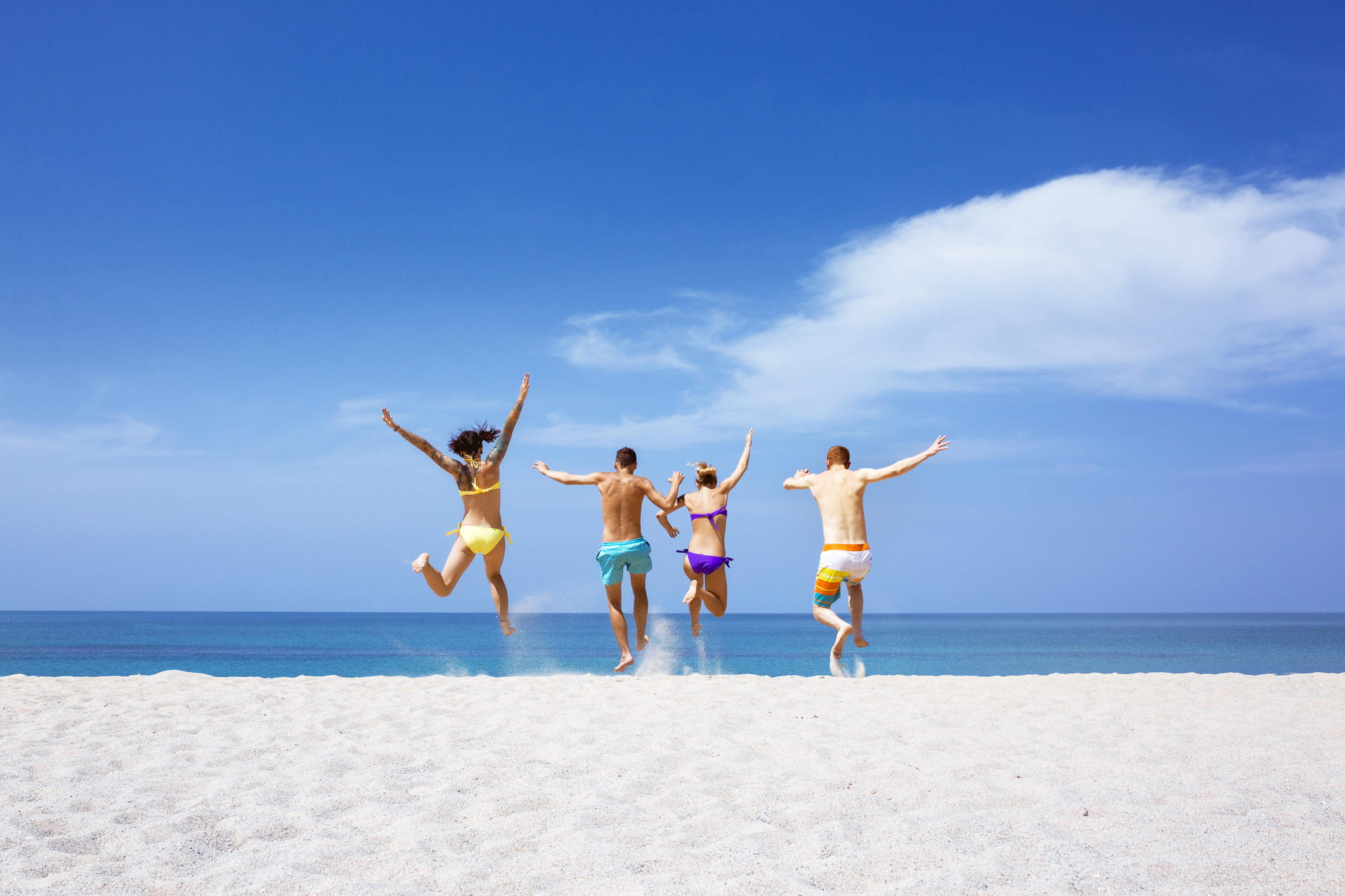 Group of people in swimsuits jumping on the beach as if celebrating