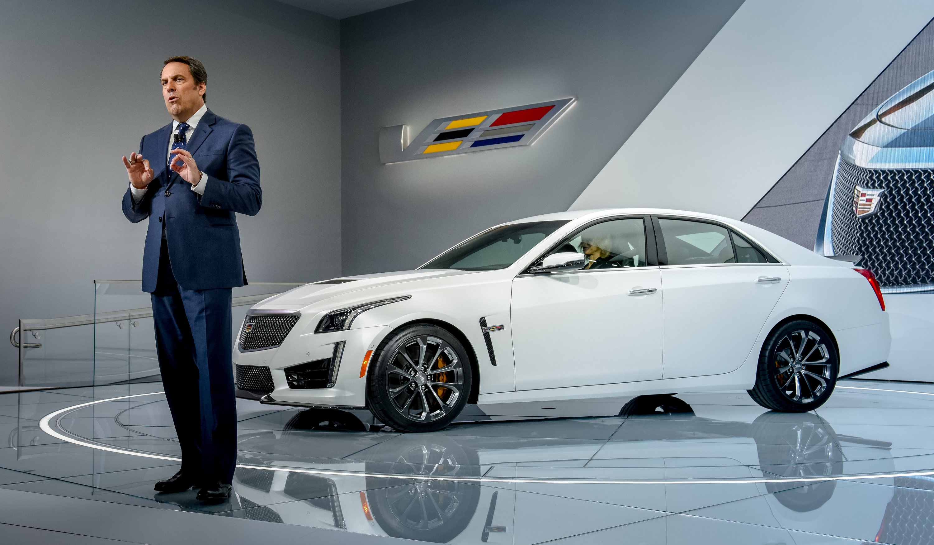 Reuss is shown standing on an auto-show stage with a while Cadillac CTS-V, a midsize high-performance luxury sedan.
