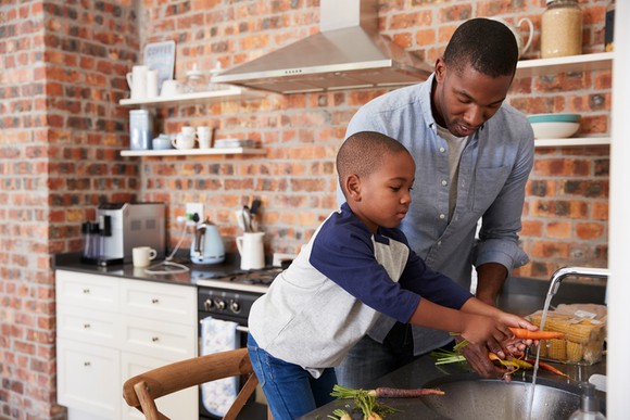 A father and son washing vegetables at the kitchen sink.