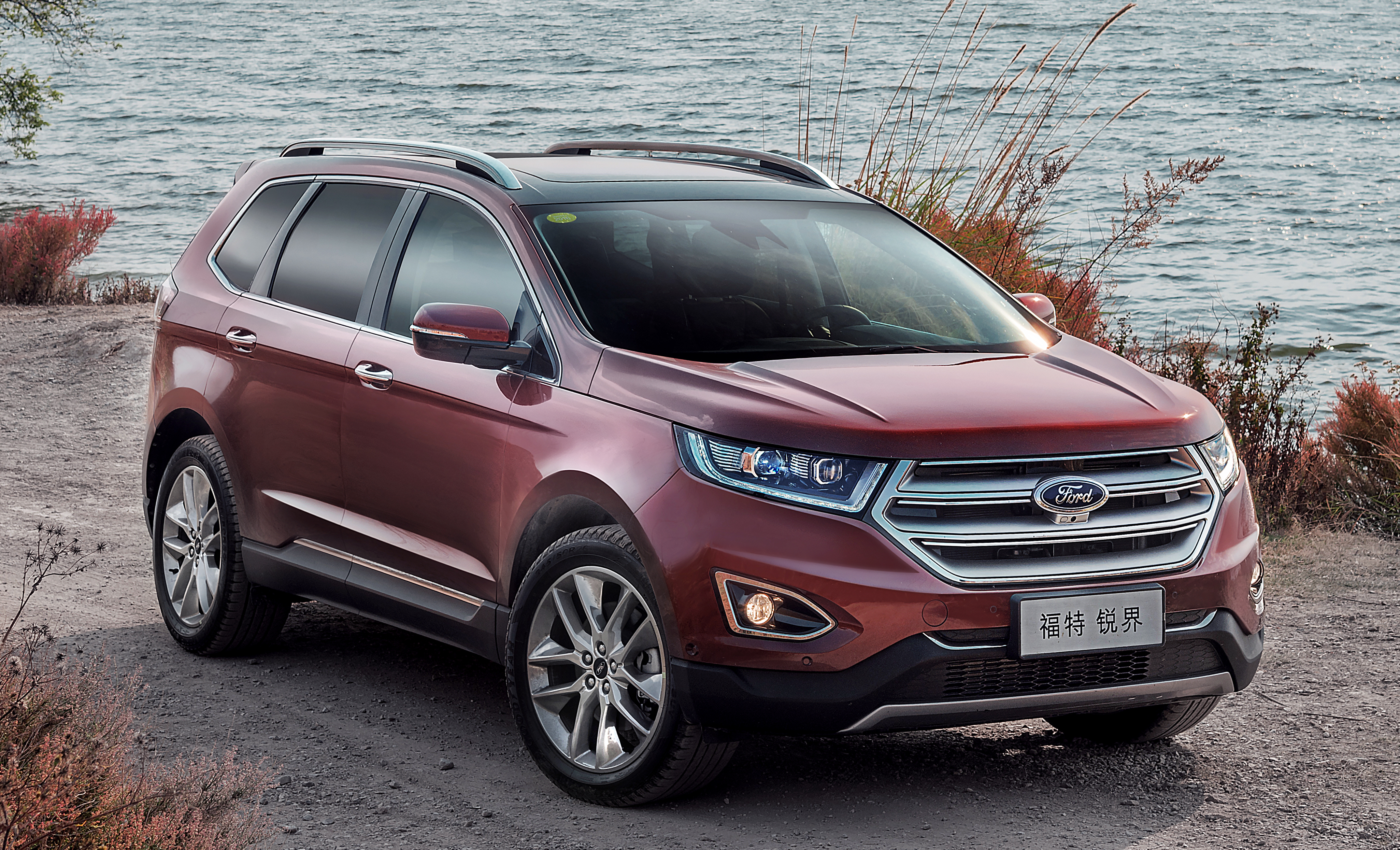 A long-wheelbase Ford Edge crossover SUV with Chinese-language license plates, parked on a waterfront.