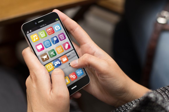 two hands holding a smartphone with many colorful app icons shown on it