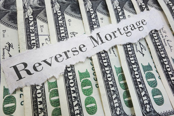 the words reverse mortgage printed on a torn piece of paper that's atop a row of hundred dollar bills