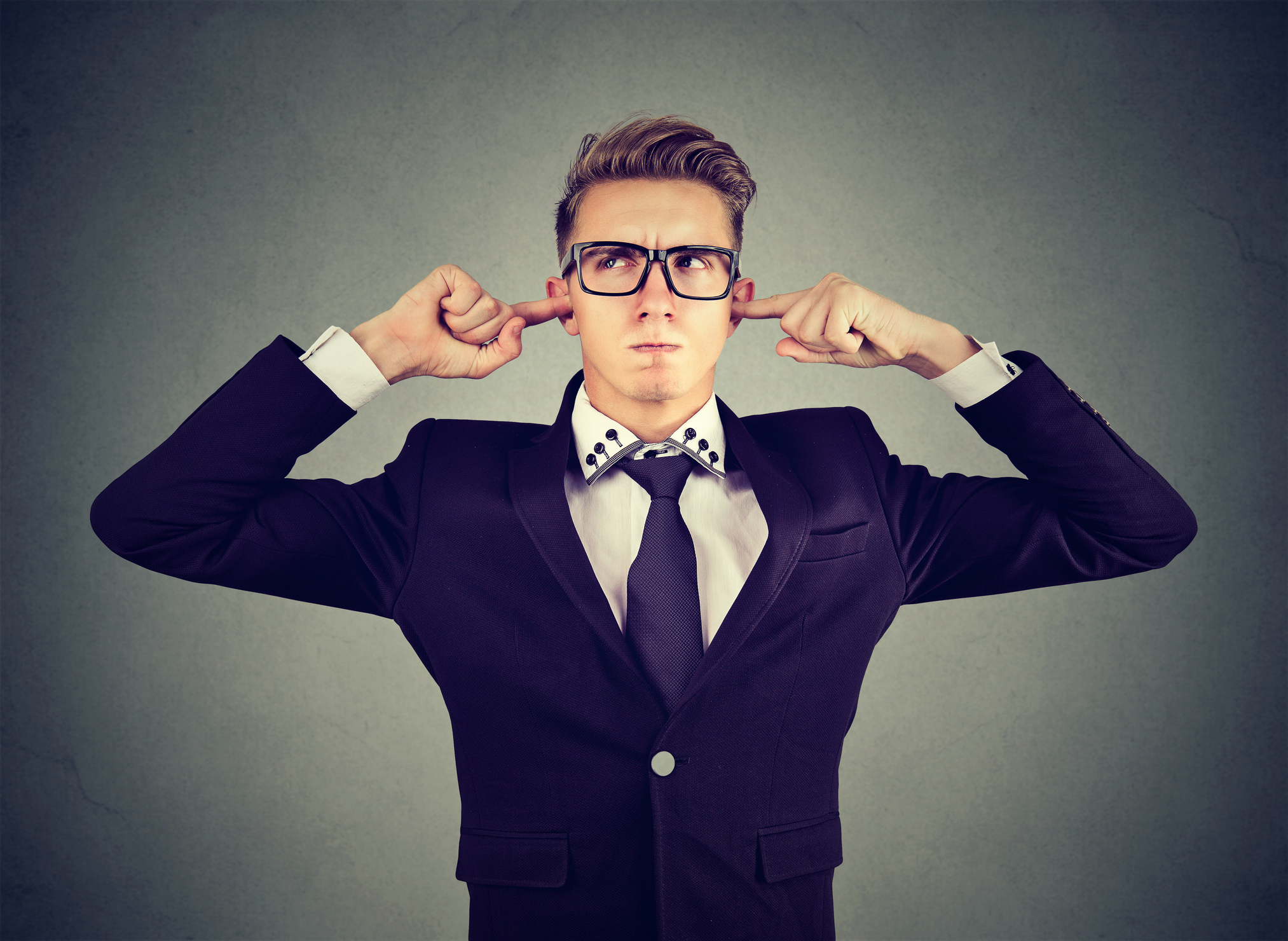 An unhappy man has his fingers in his ears.