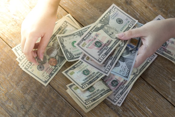 Hands counting money on a wooden table.