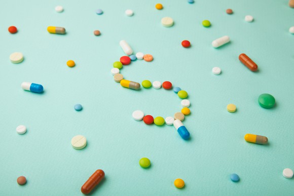 Different colored pills with some arranged in the shape of a dollar sign
