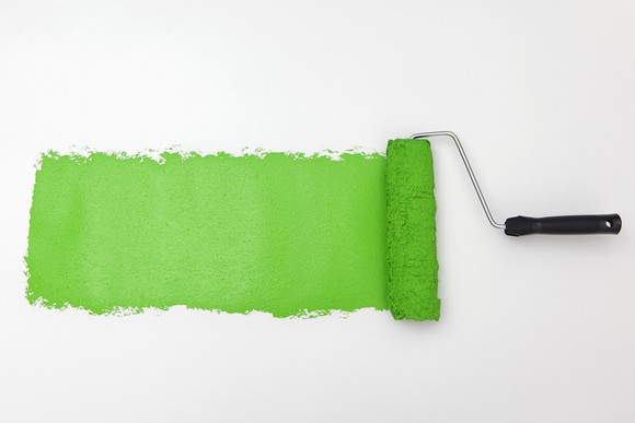 A paint roller adding lime green paint to a white wall