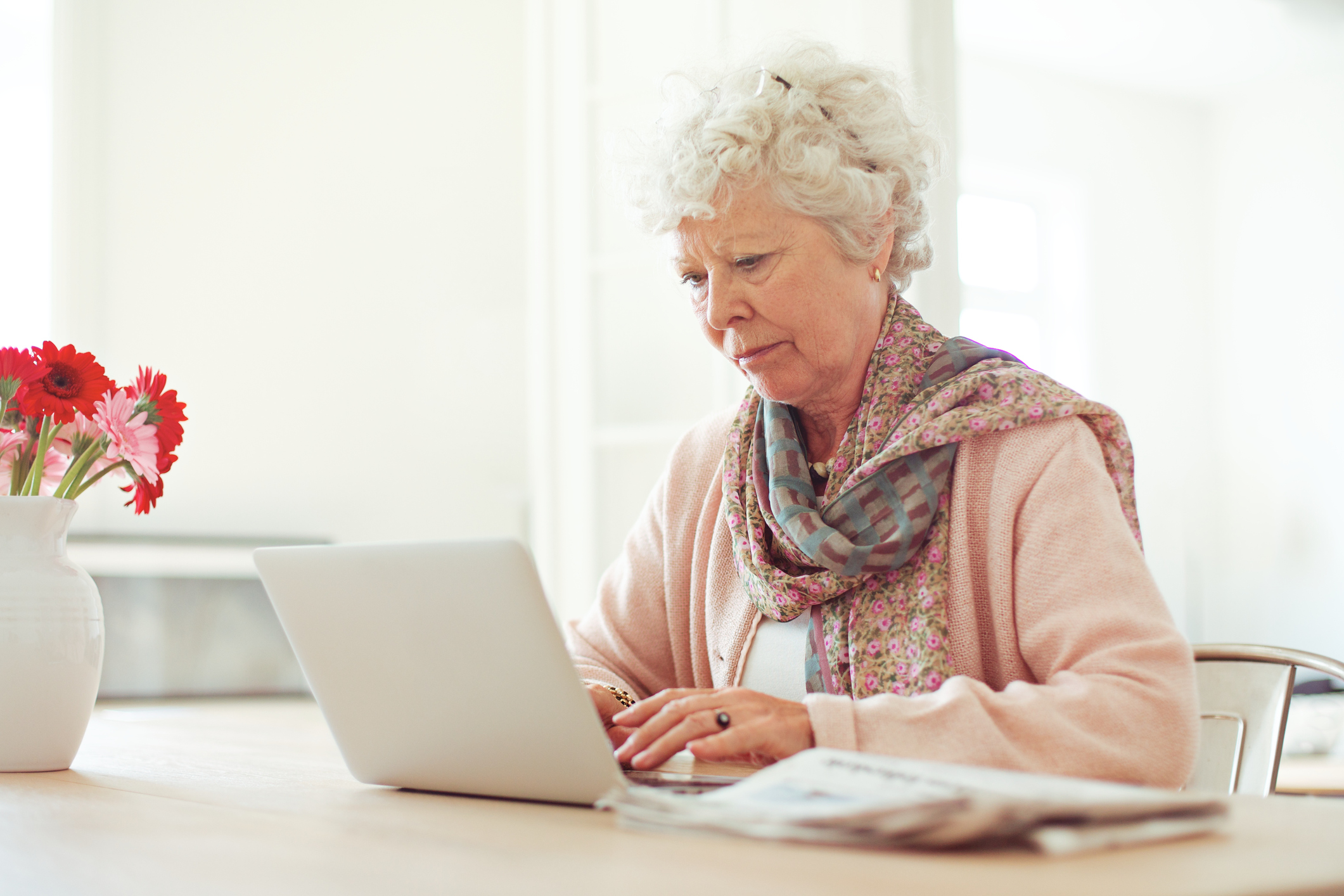 Older woman sitting at a table while typing on a laptop