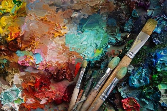 A close-up of a painting and paintbrushes. Various colored paints are displayed painted onto a canvas.