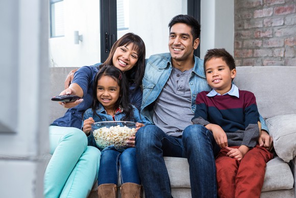 A smiling family sitting on the couch eating popcorn and watching TV.