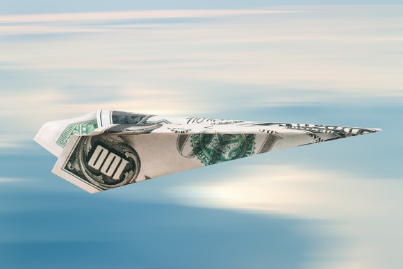 Paper airplane made of a hundred dollar bill, in flight against a blue sky