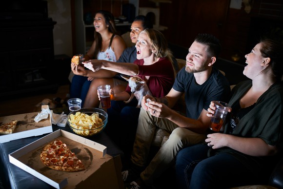 Friends watching TV and eating pizza together.