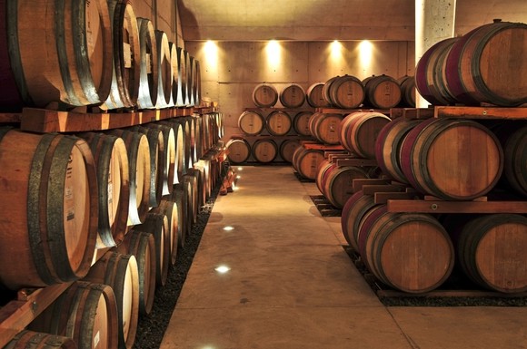 Rows of wooden wine barrels in well-lit cellar.