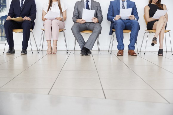 Multiple people sit in a waiting room holding papers.
