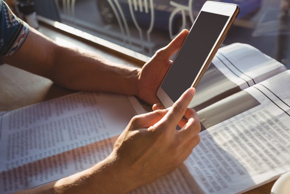 A person holds a tablet over a newspaper.