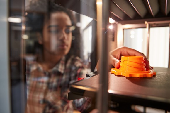 A person 3D printing an orange part.