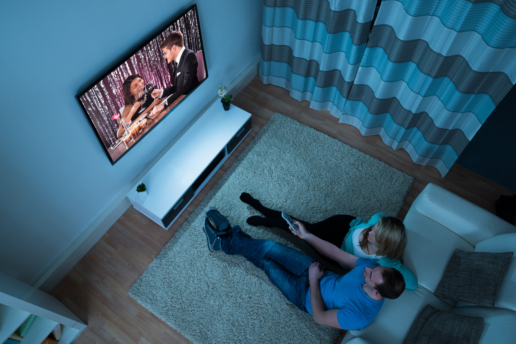 Couple watching TV in a darkened living room, seen from the floor above