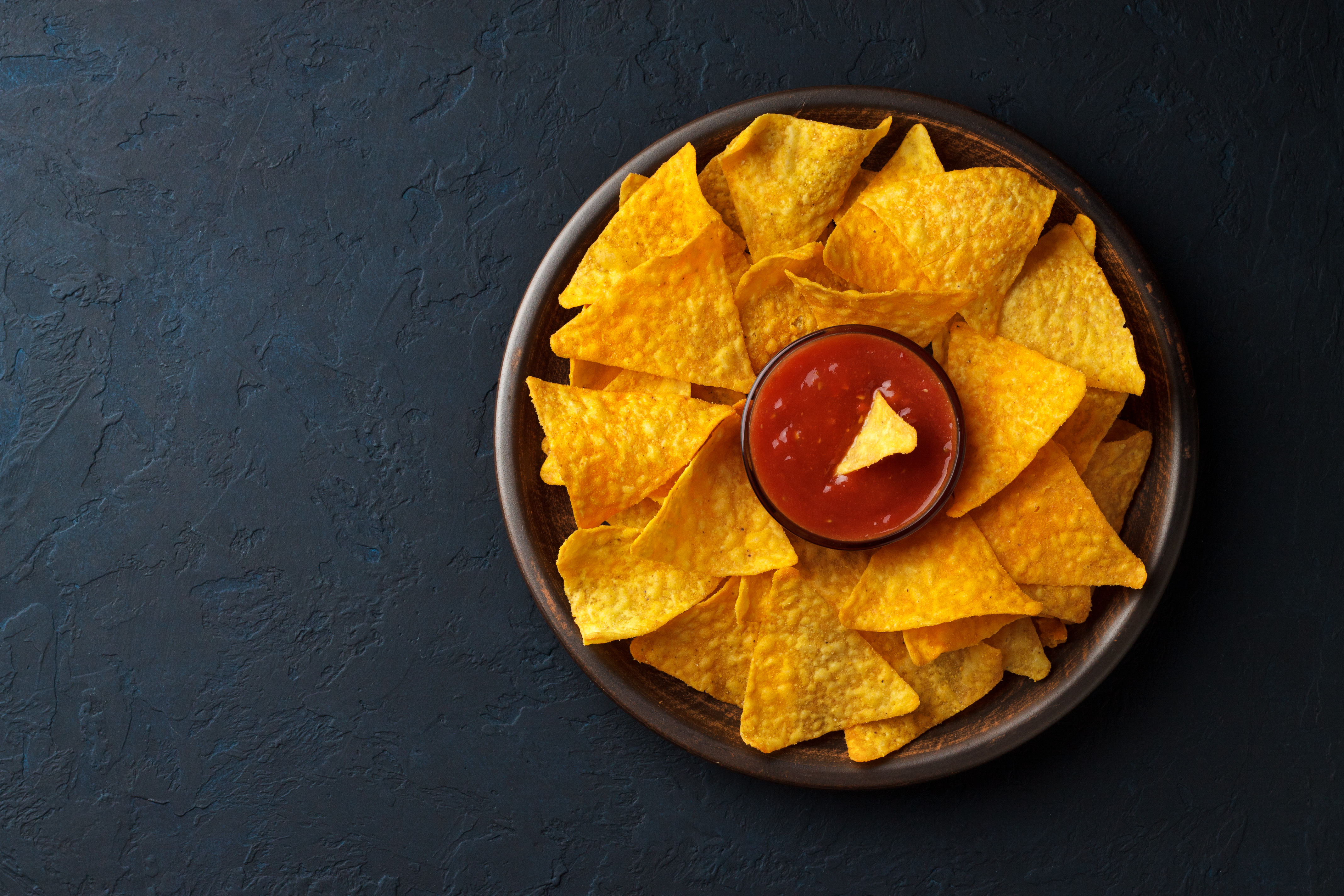 Bright yellow tortilla chips in a brown bowl with salsa in the center.