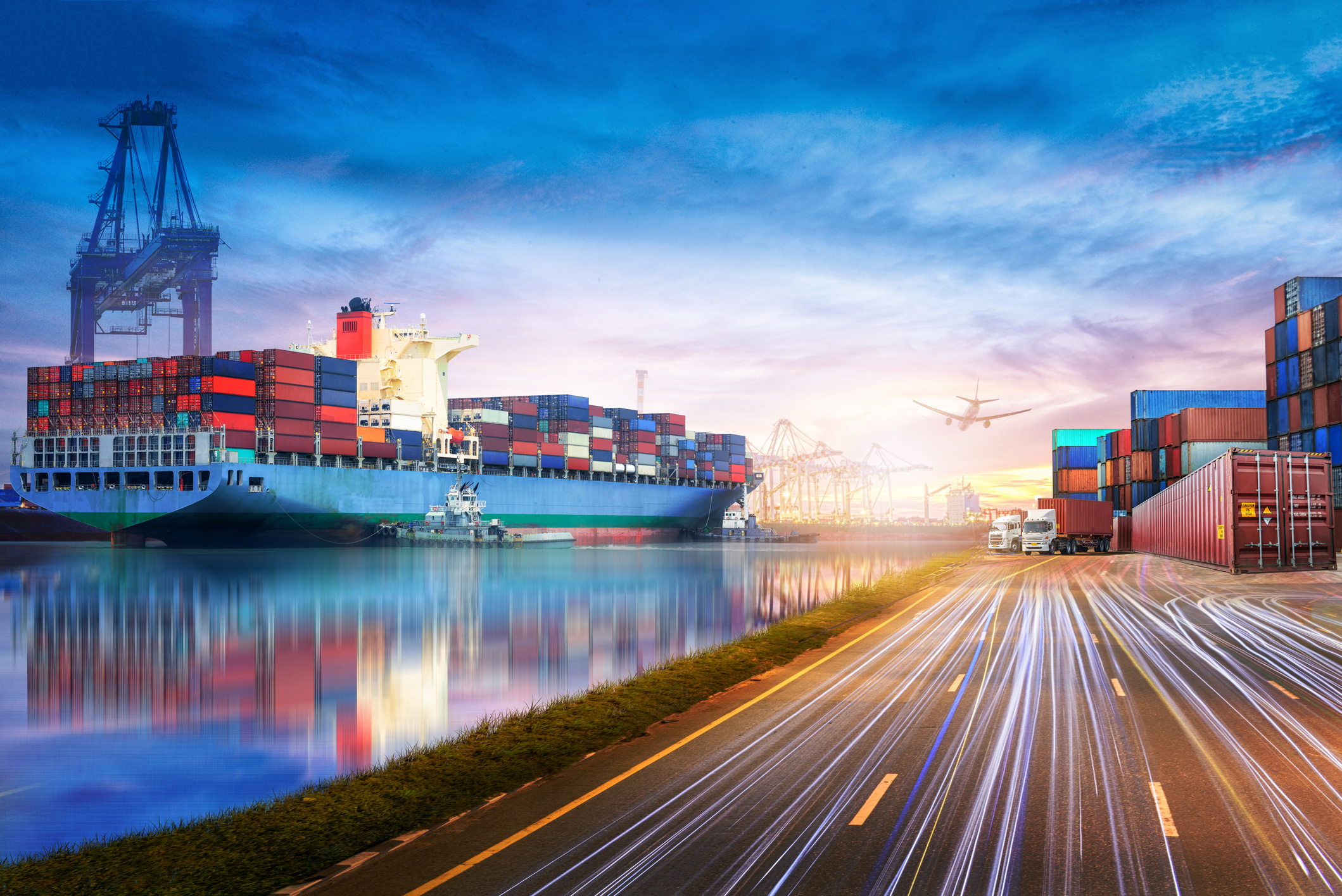 A cargo ship in a port next to trucks on a highway