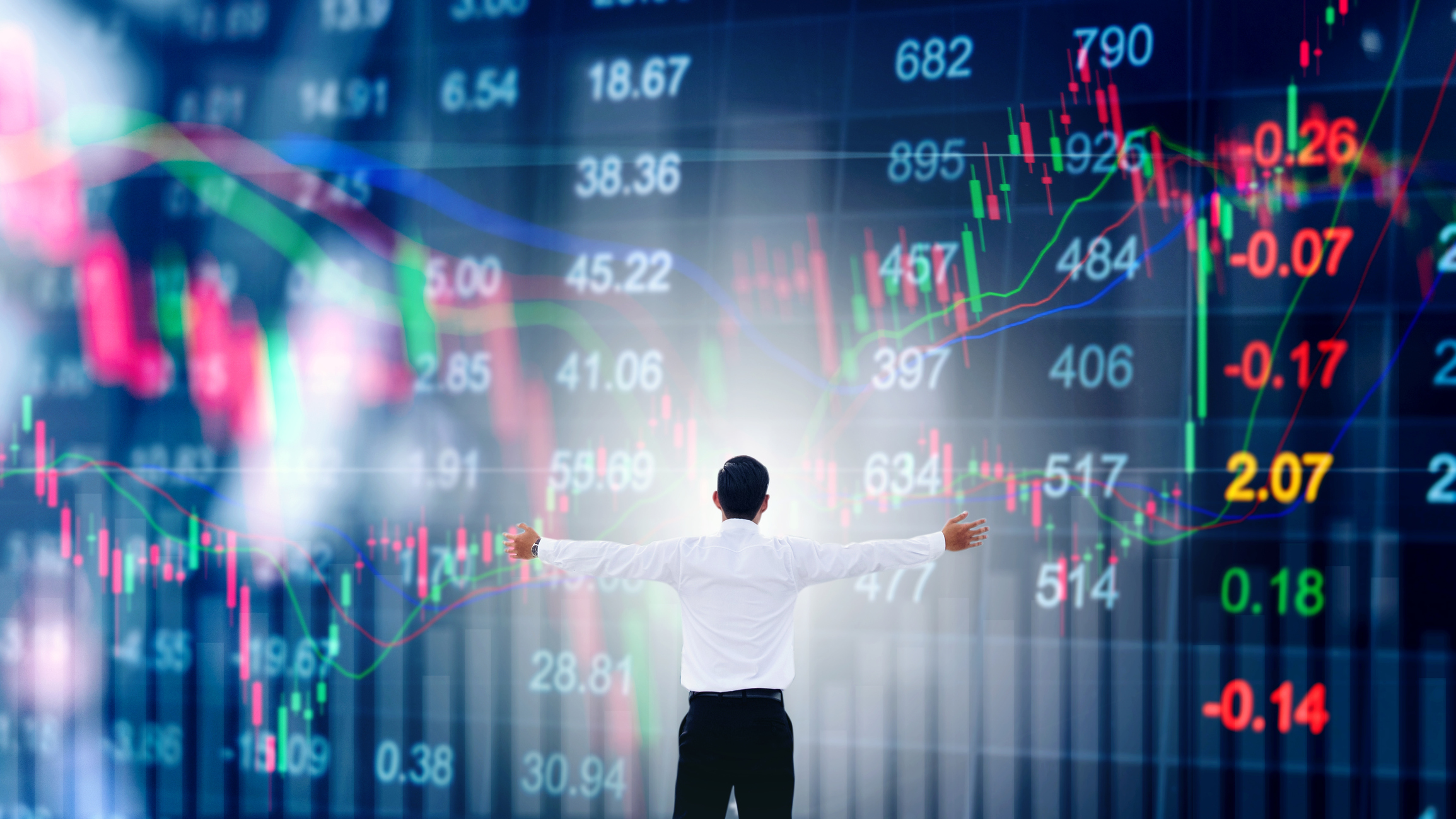 Man with outstretched arms looking at giant screen with stock information