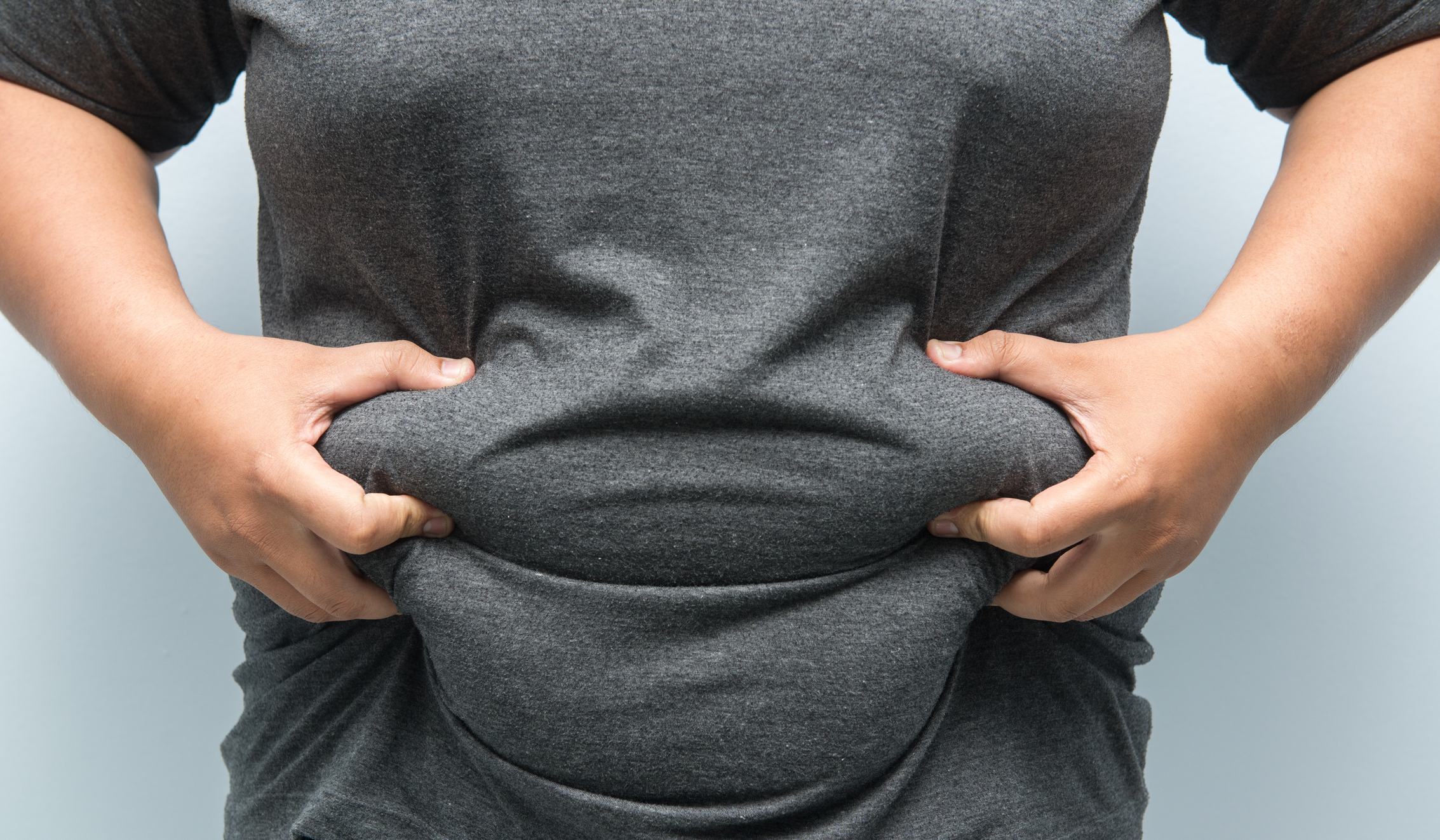 A person pinching fat on their belly through a T-shirt
