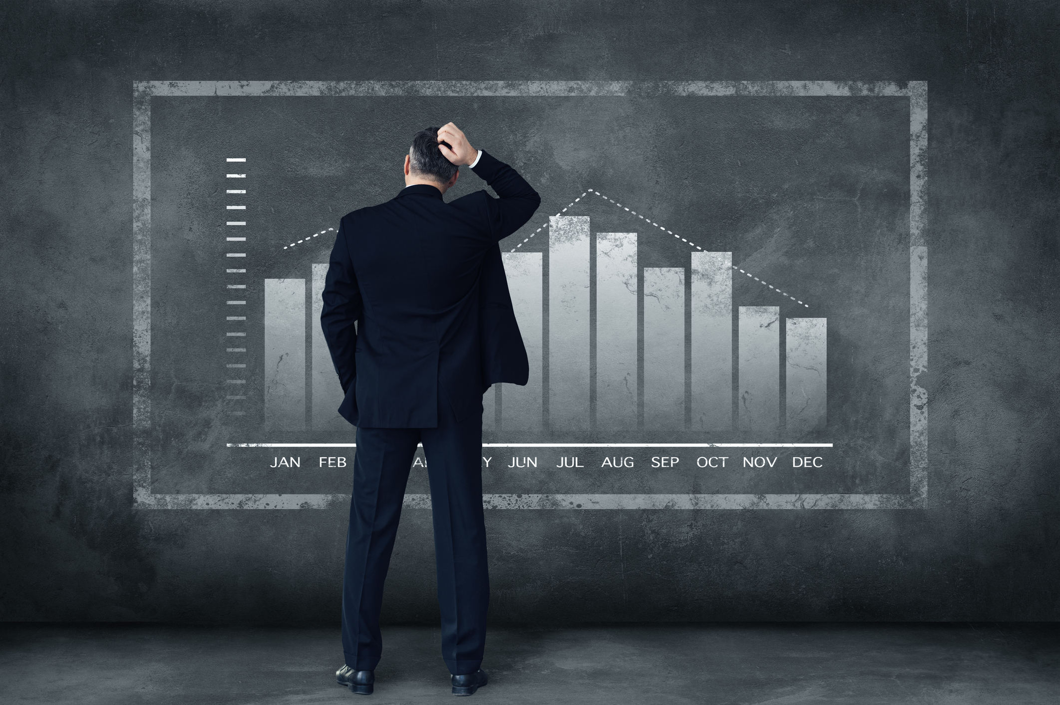 A man scratching his head while looking at a chart on a chalkboard
