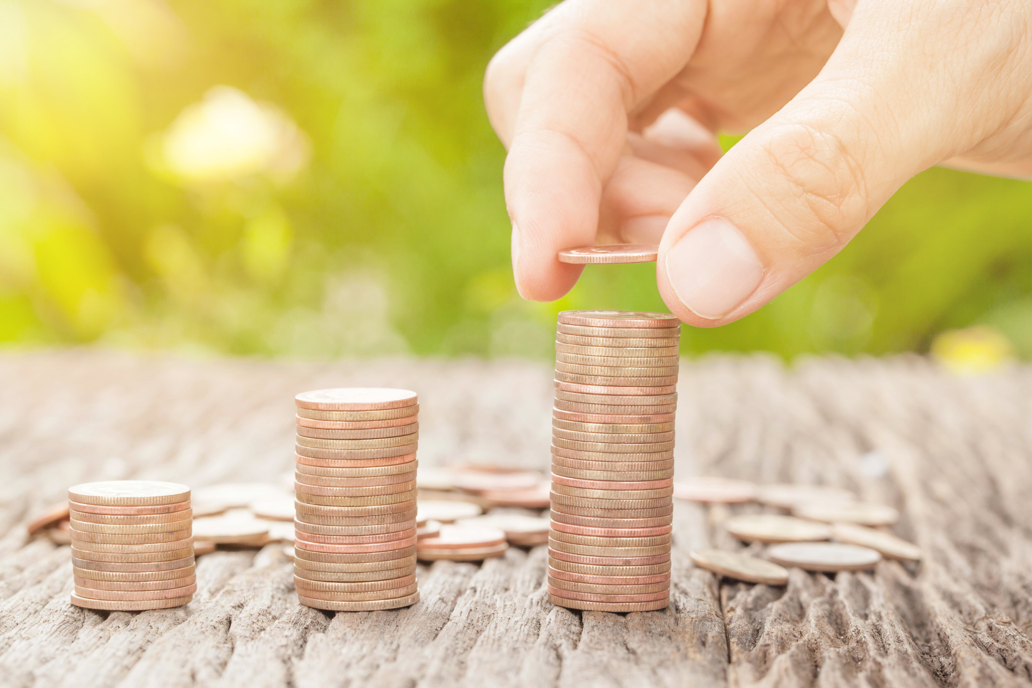 A hand pointing another coin on a rising stack.