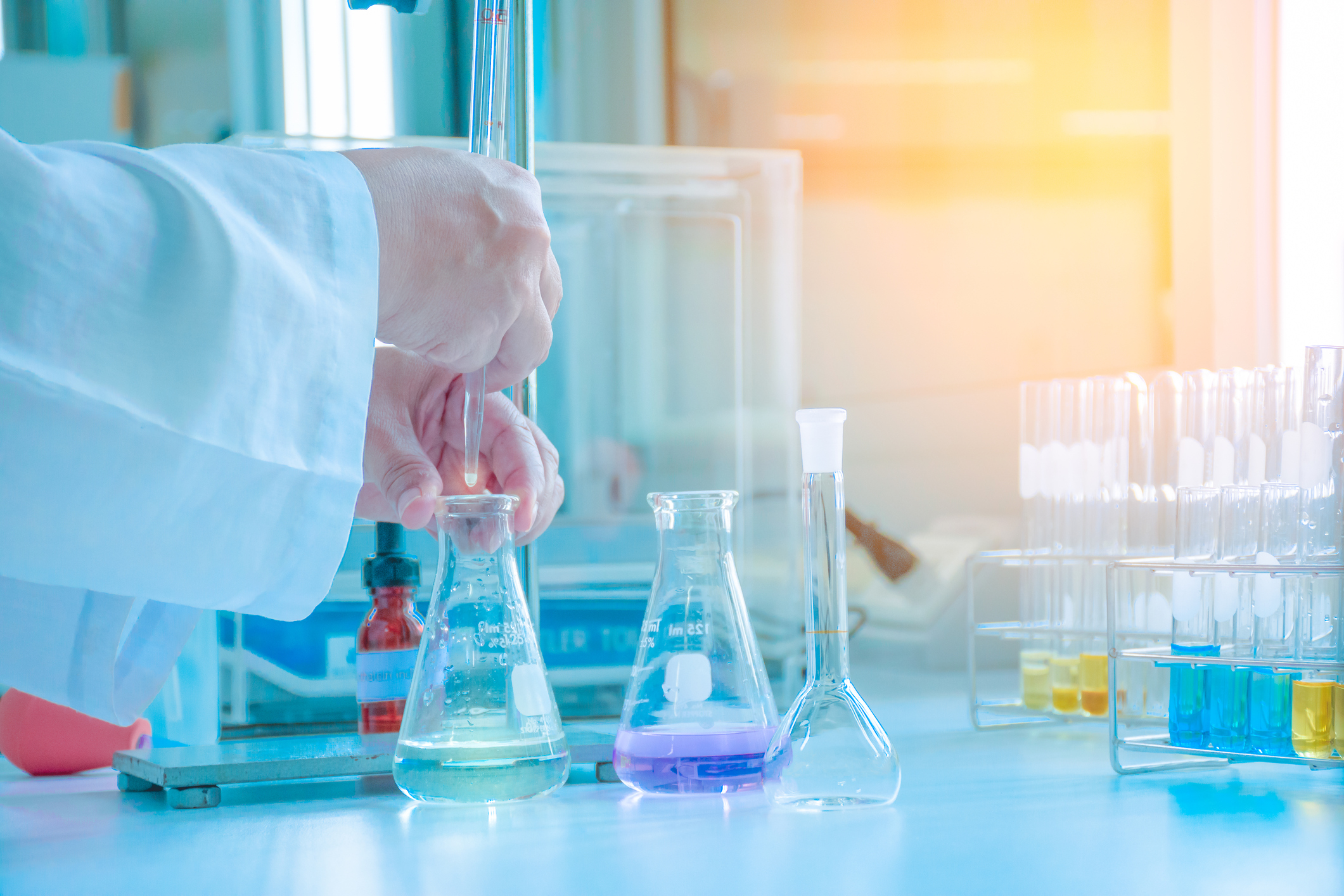 Chemist adding liquid to flask on a table with multiple flasks