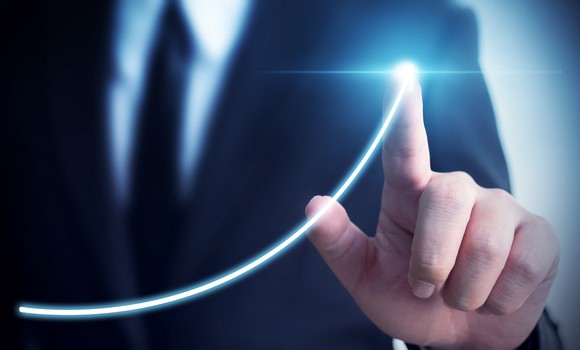 A hand traces a bright line on a chart higher. 