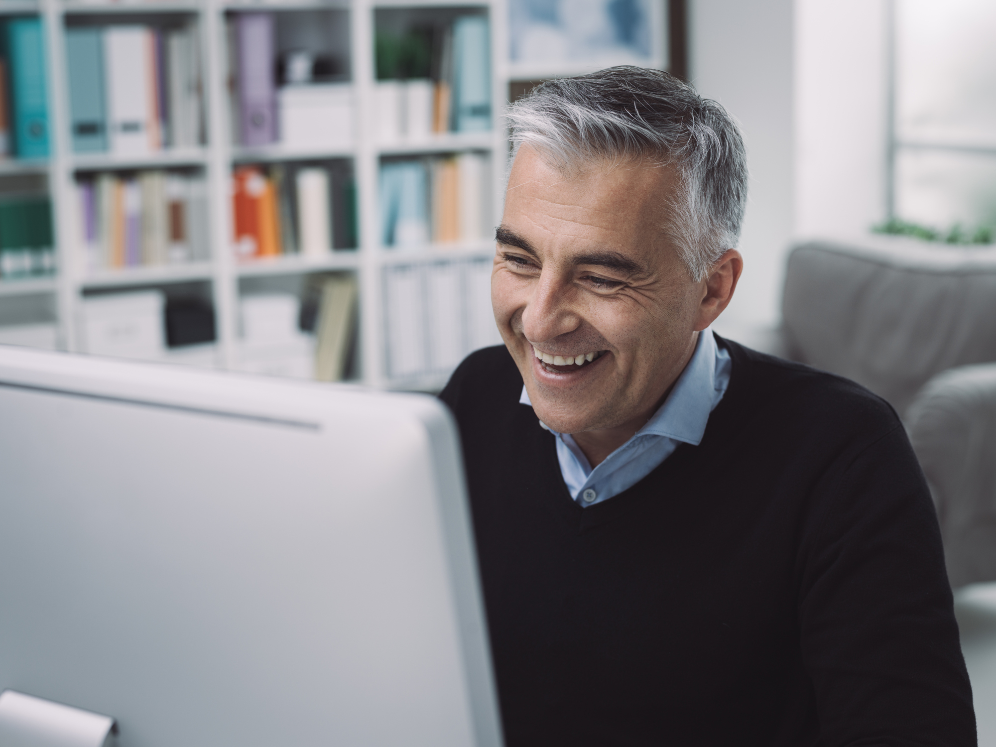 Smiling gray-haired man at laptop.