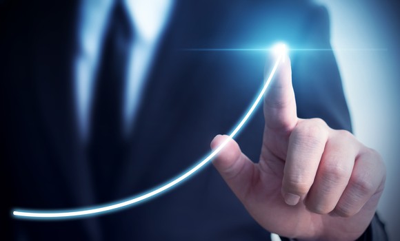 A man in a suit drawing an upward arrow with his finger.