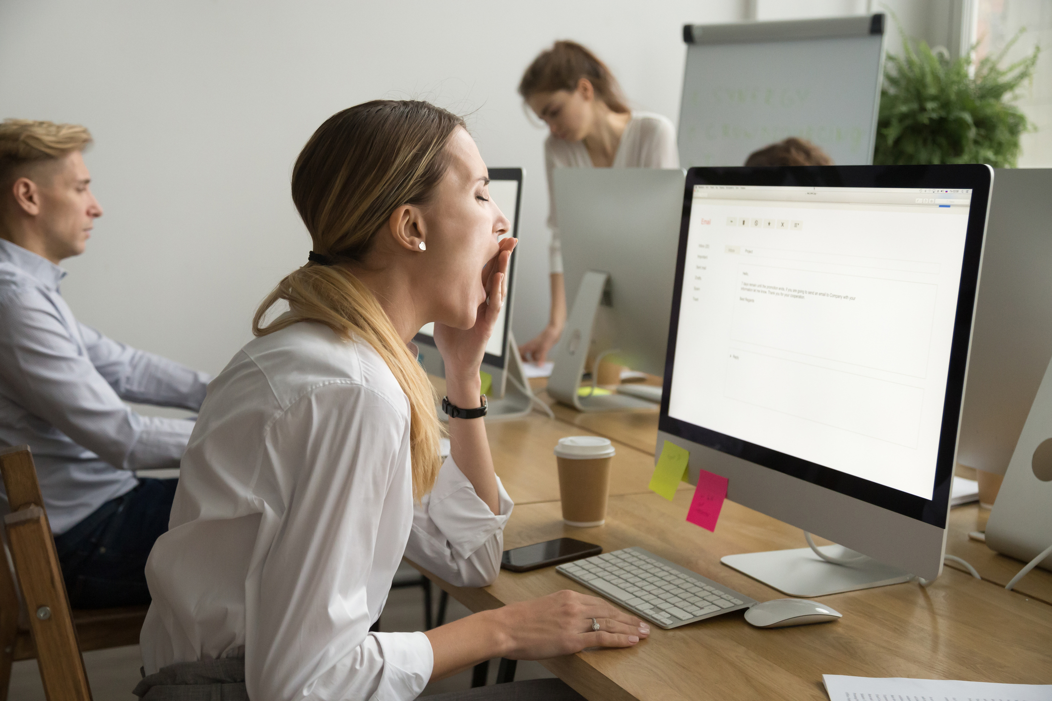 A woman sitting in front of a computer stifles a yawn.