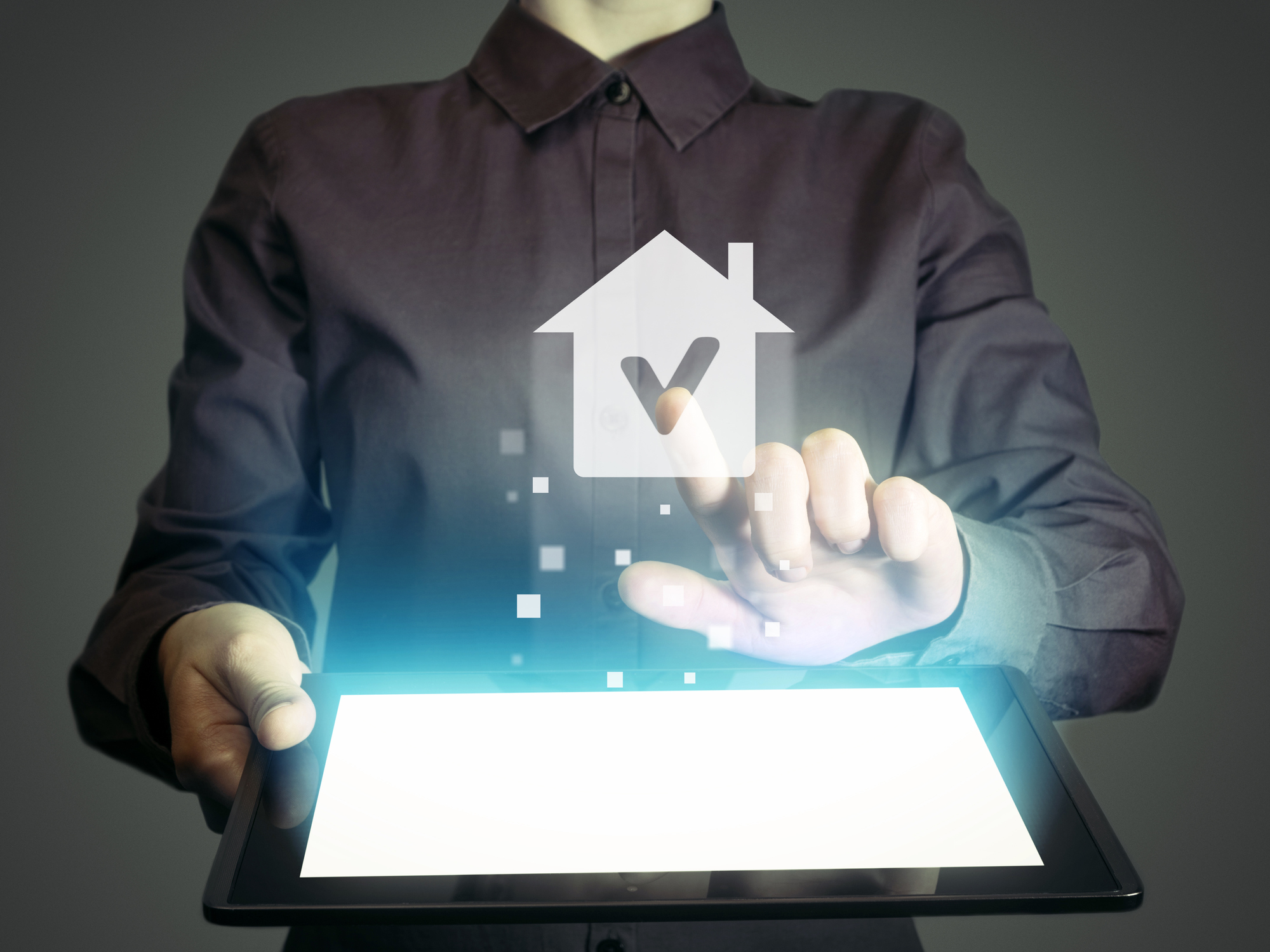 A person holding a tablet and pressing a digital image of a house projected above it.