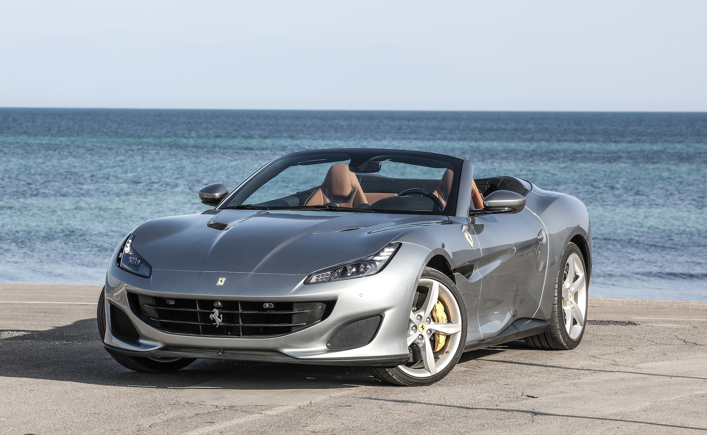A silver Ferrari Portofino, a sharply-styled four-seat convertible sports car, parked on a waterfront.