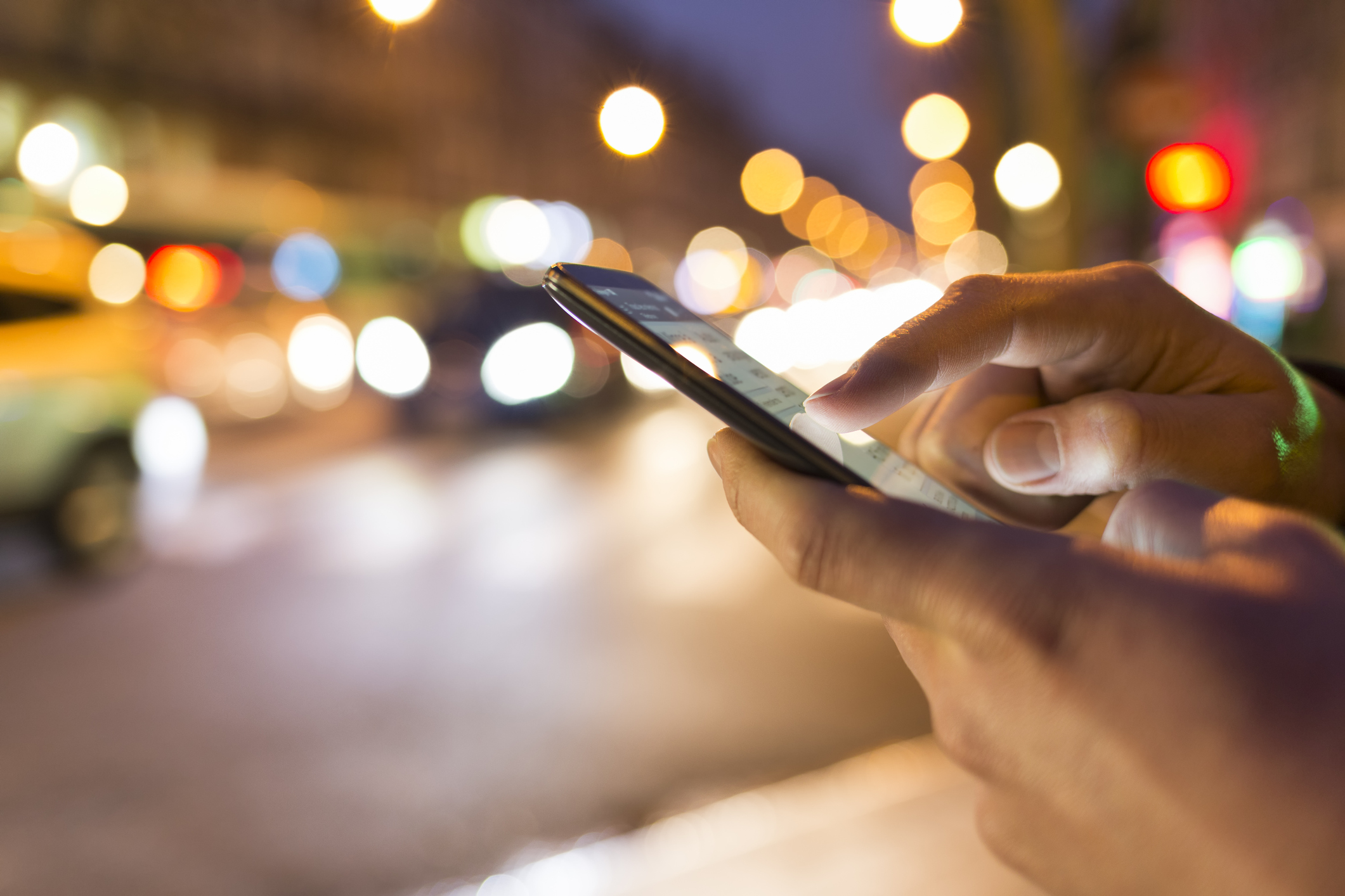Up close picture of hand with smartphone with traffic in background.