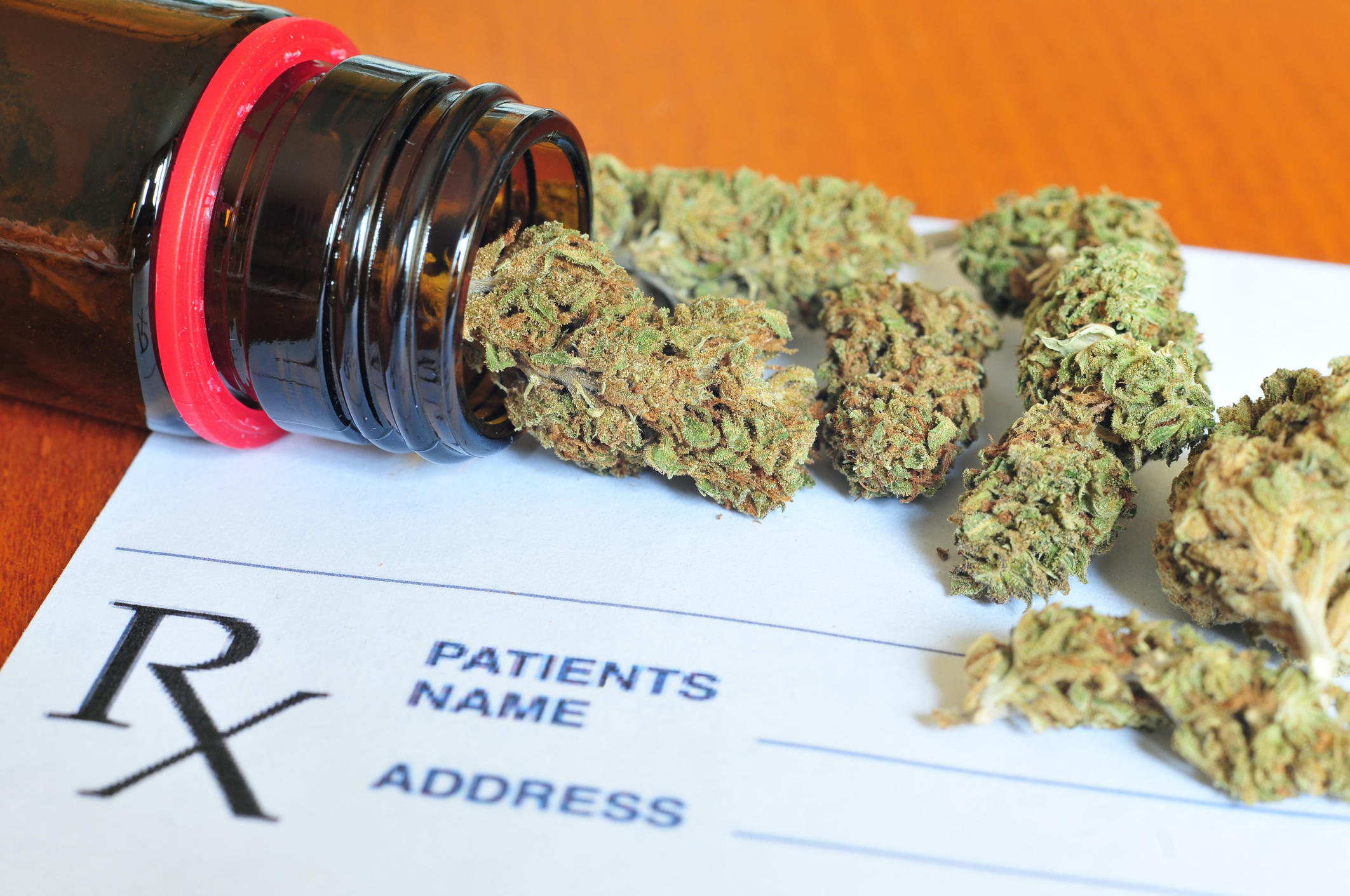 Marijuana buds spilling out of bottle on top of a prescription form