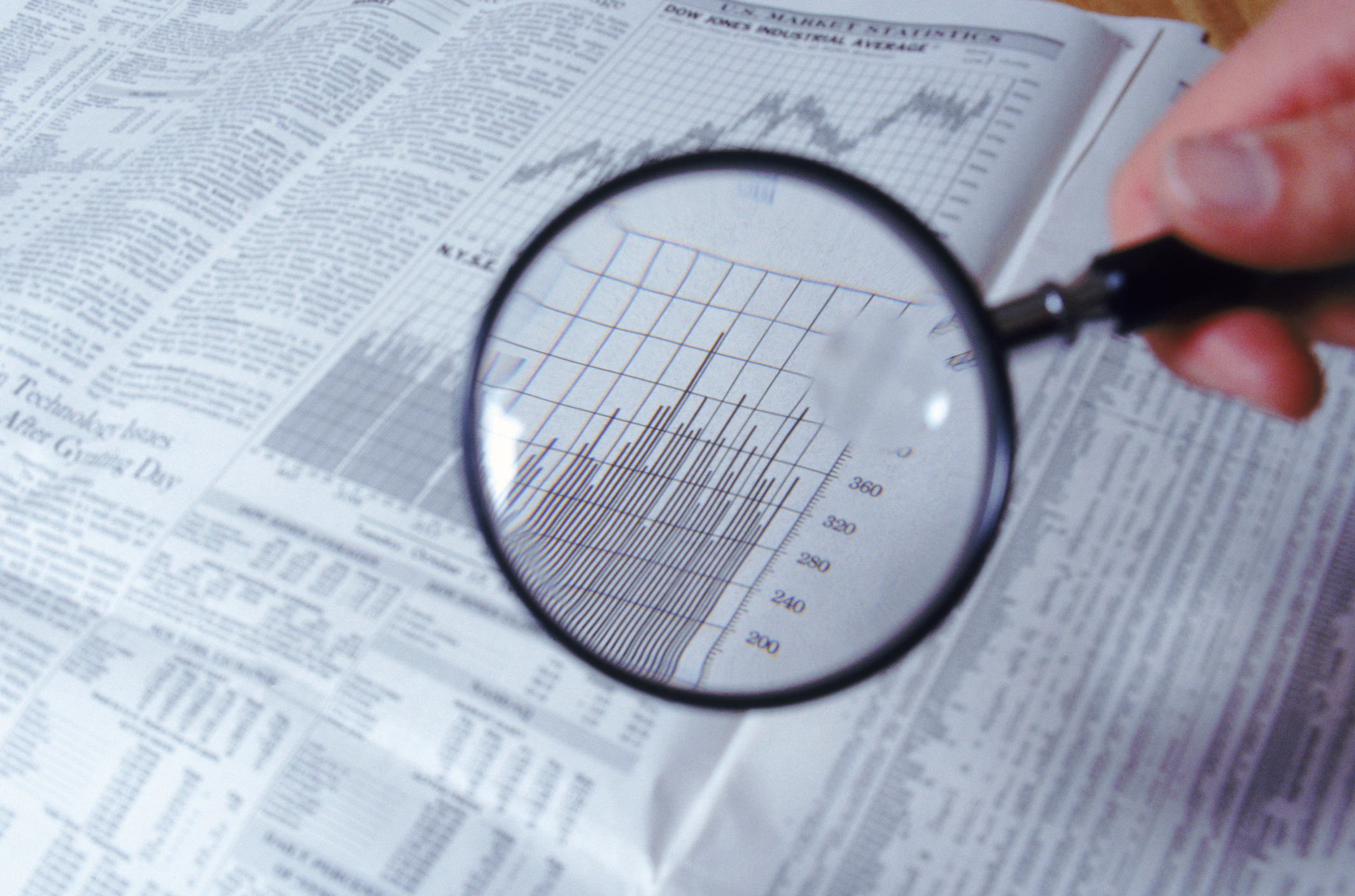 A magnifying glass held over a financial newspaper.