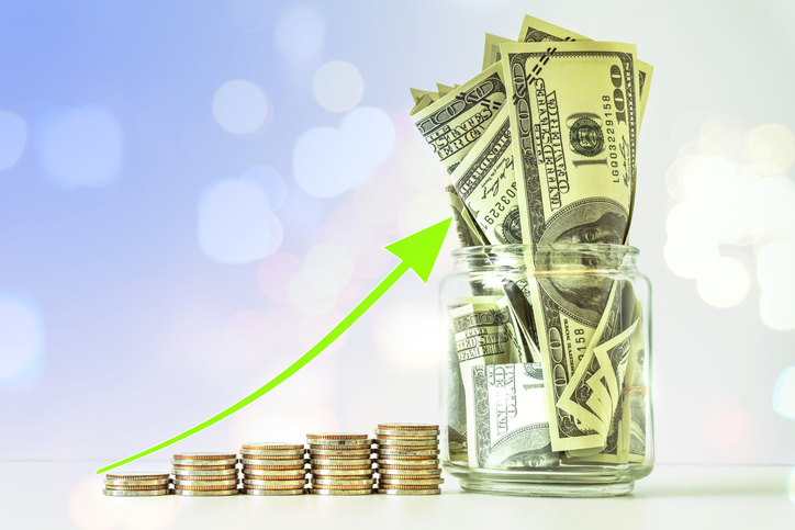 Successively taller columns of coins, a green arrow above them, and a jar with $100 bills stuffed in it.