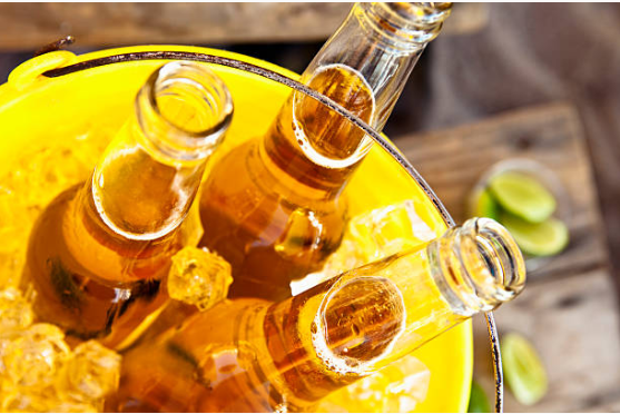 A metal bucket filled with ice and three open glass bottles of beer. The bucket sits on a wooden table scattered with pieces of lime.