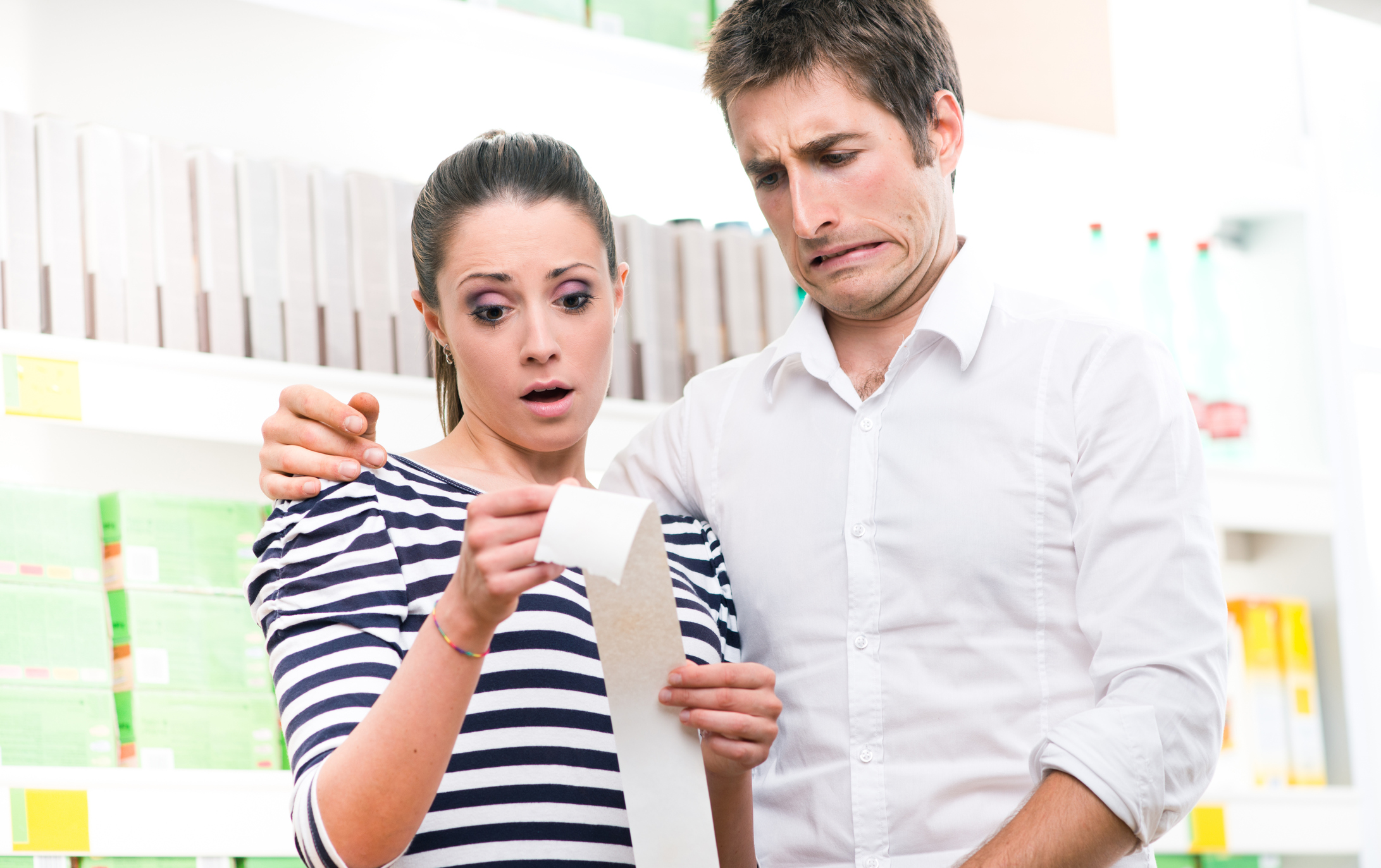 A young couple concerned by high prices on their store receipt.