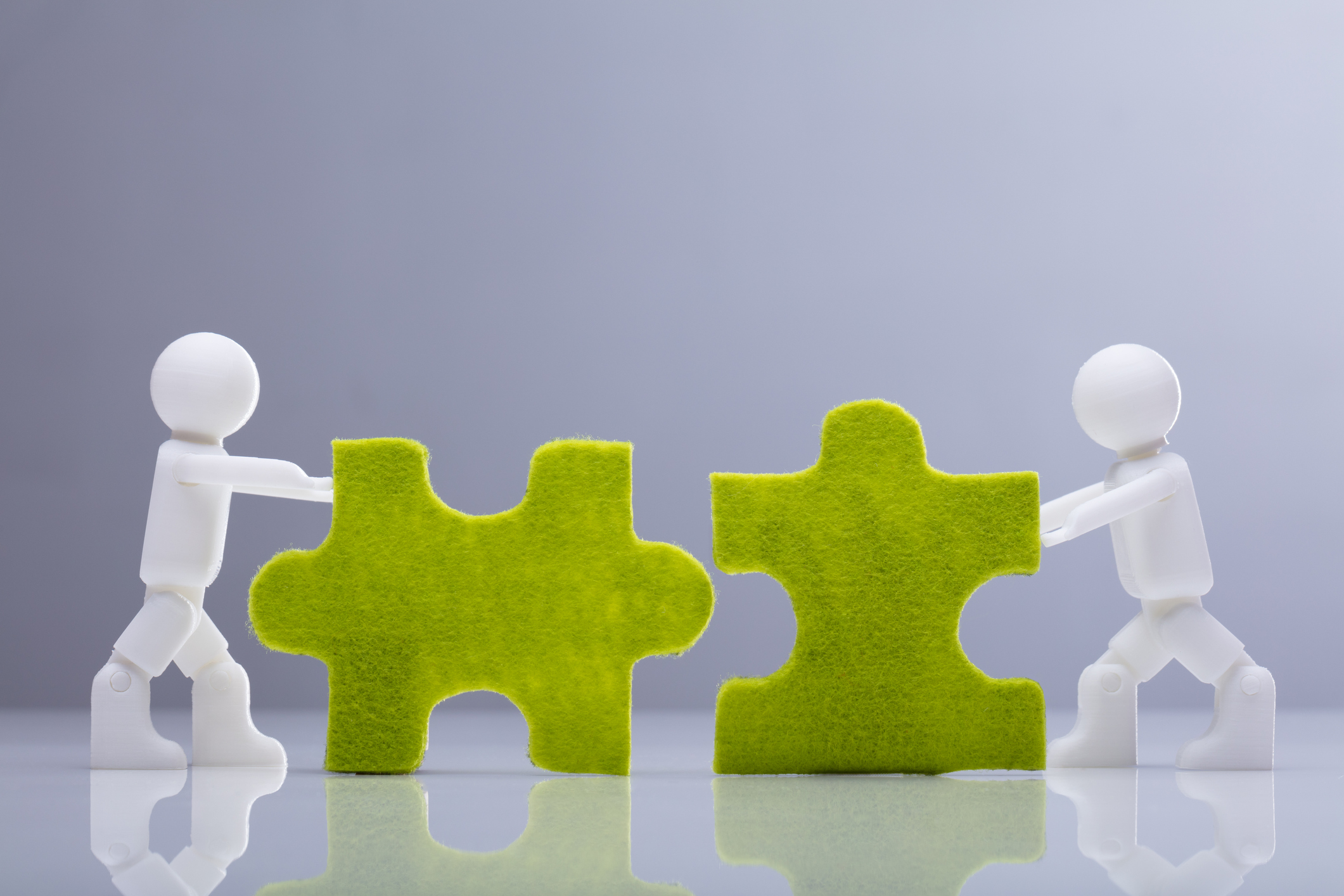 Mini human figures pushing green jigsaw pieces