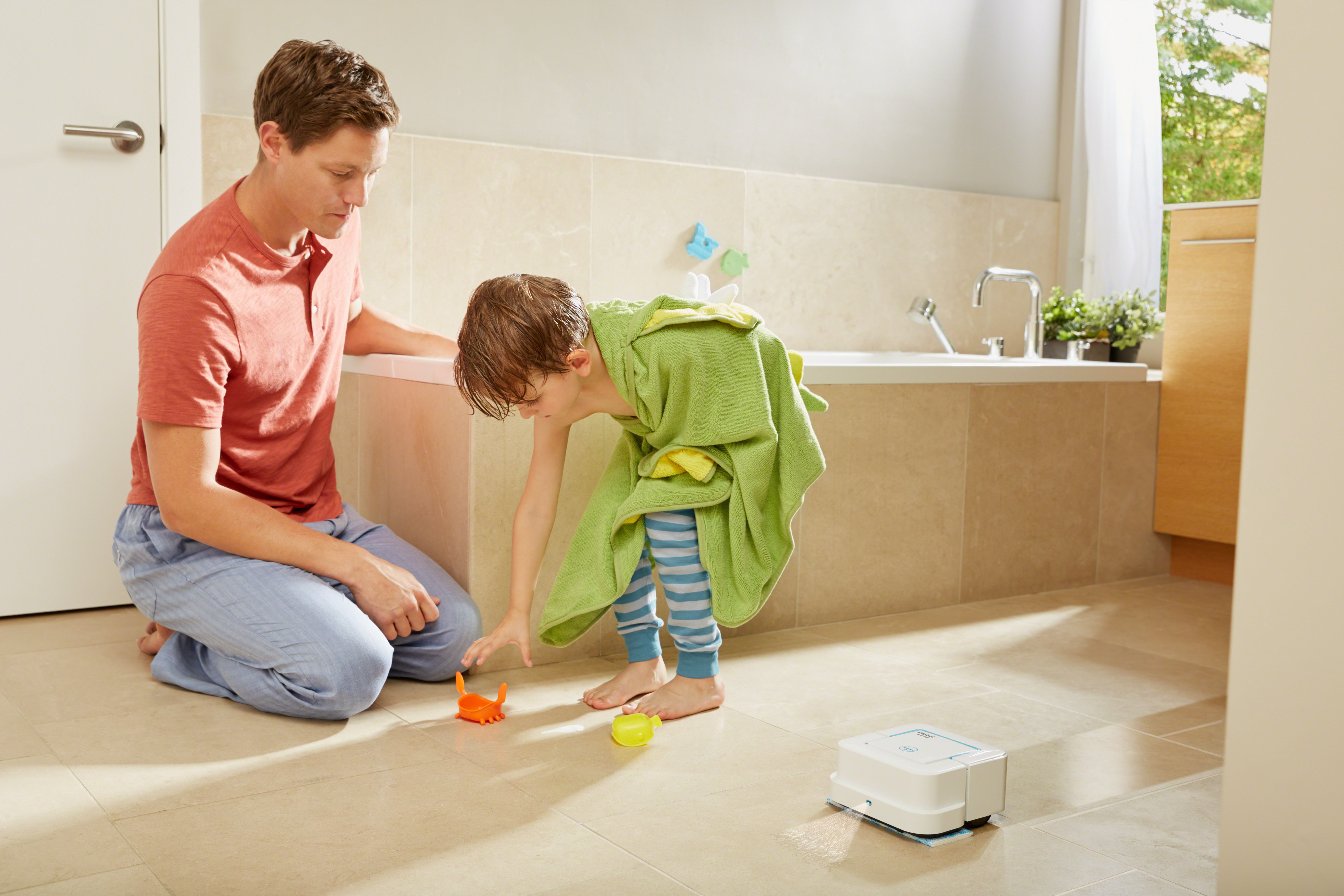 iRobot Braava jet robot cleaning a bathroom floor with a father and son in the background.